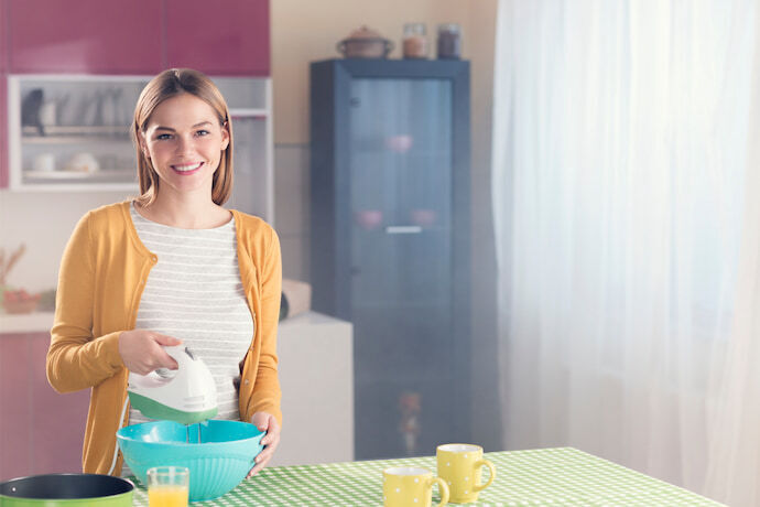 Mulher usando batedeira em uma tigela azul na cozinha.