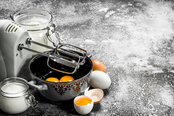 Par de batedores simples, recipiente com ovos e trigo sobre uma mesa.