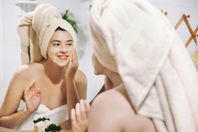 Mulher feliz com toalha de banho fazendo massagem facial.