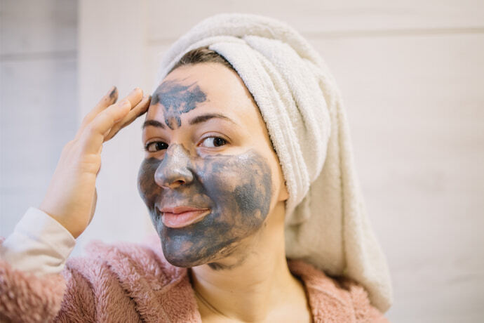Mulher utilizando um creme de esfoliação no rosto de cor cinza.