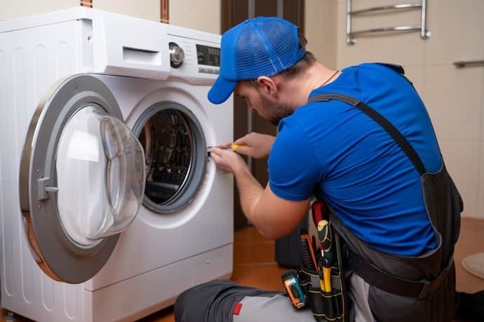 Homem de roupa azul instalando uma máquina de lavar em casa.