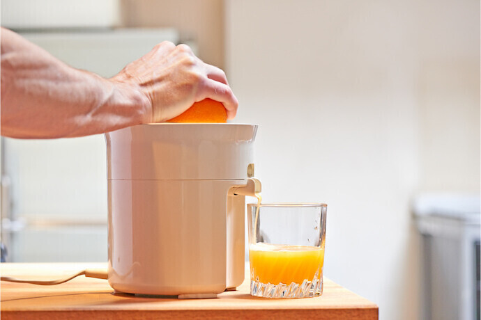 Mãos pressionando a laranja em um espremedor de suco