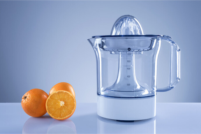 Espremedor de frutas transparente e ao lado laranjas