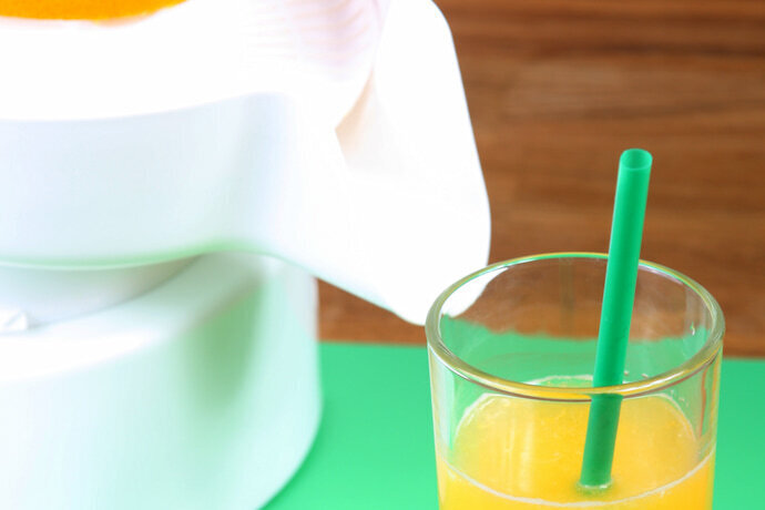 Espremedor de frutas e um copo com suco de laranja e um canudo