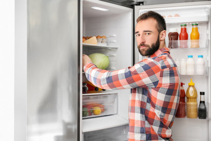 Homem escolhendo alguma comida na geladeira em casa.