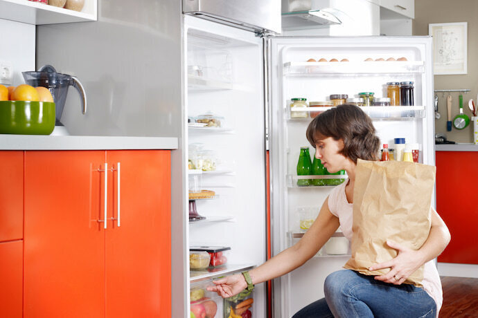 Mulher organizando os alimentos na geladeira.