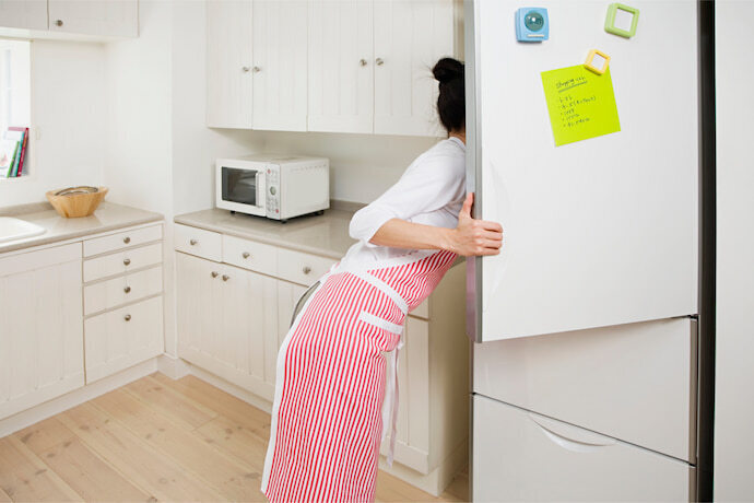 Mulher de avental olhando a parte interna da geladeira.