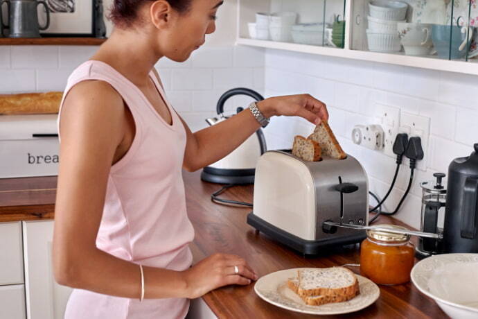 Mulher tirando as fatias de pães da torradeira elétrica