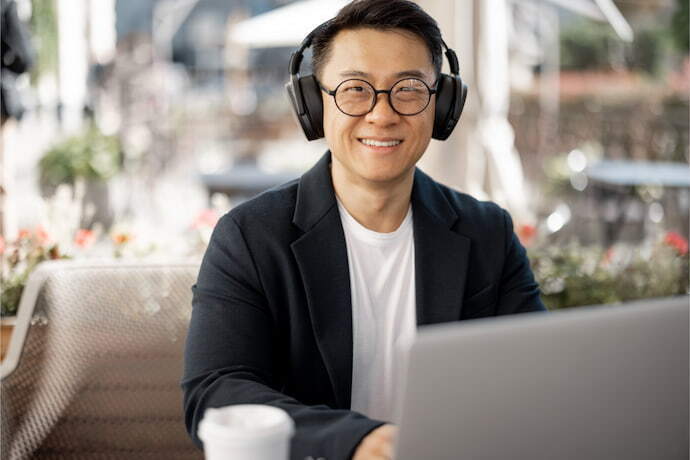 Homem com fones de ouvido trabalhando no laptop em uma cafeteria.