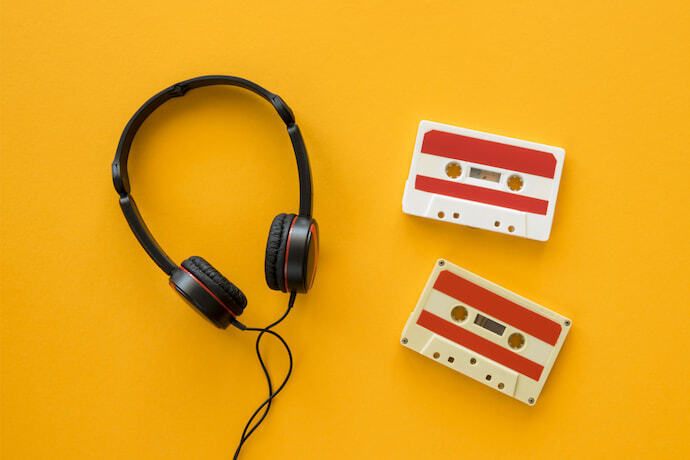 Close-up de fone supra-auriculares e duas fitas cassetes em um fundo amarelo.