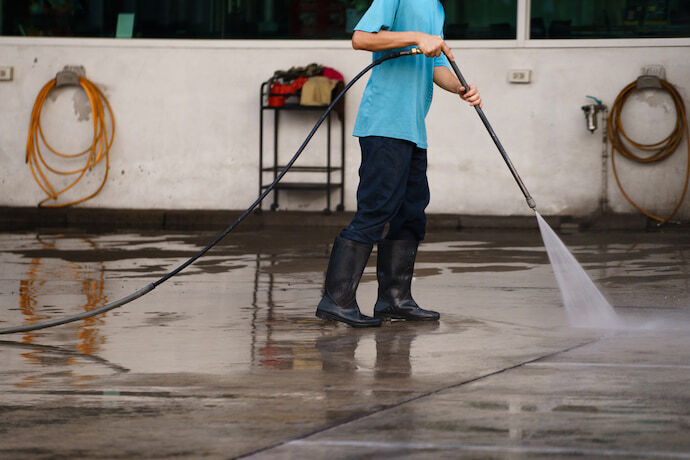 Um homem com lavadora de alta pressão limpando o chão 