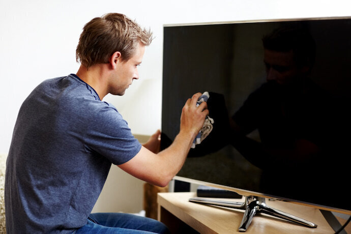 Homem limpando a Smart TV com um pano seco.