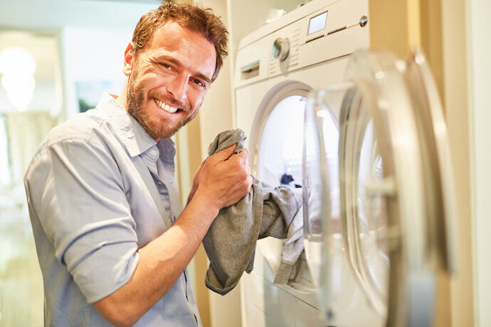 Homem sorrindo mexendo em roupas na máquina
