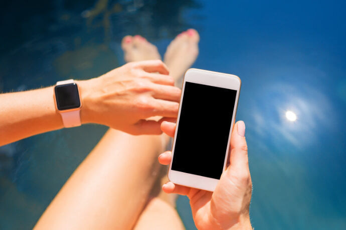 Mulher próxima de uma piscina com smartband e celular