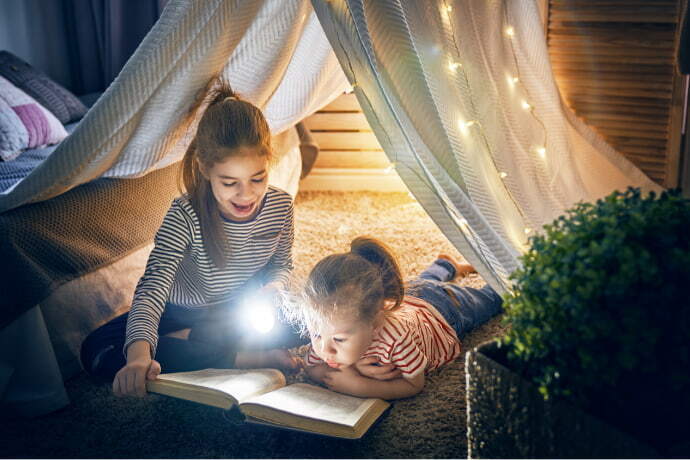 Crianças lendo um livro com o auxílio da lanterna.