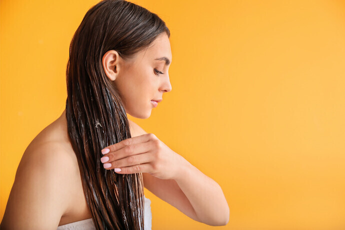 Mulher aplicando creme hidratante no cabelo em um fundo laranja.
