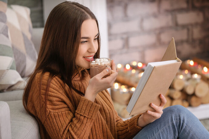 Mulher bebendo chocolate quente e lendo um livro em casa.