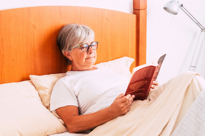 Mulher idosa na cama lendo um livro.
