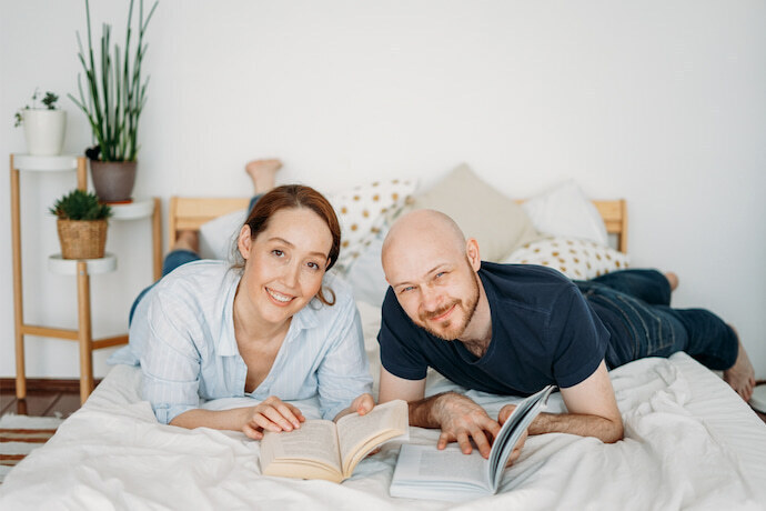 Casal sorridente lendo livros na cama.