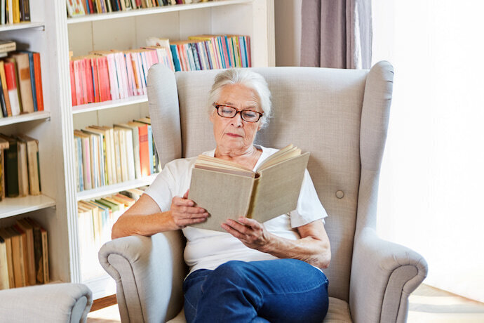 Mulher idosa lendo um livro na poltrona.