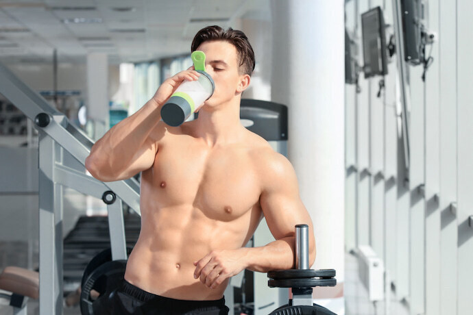 Homem desportista bebendo whey protein na academia.