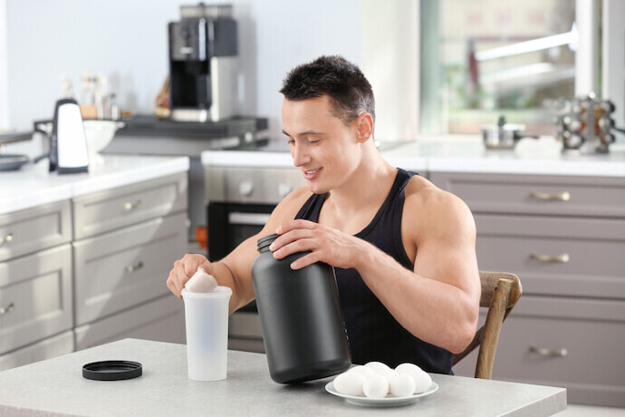Homem desportista preparando um shake de proteína na mesa.