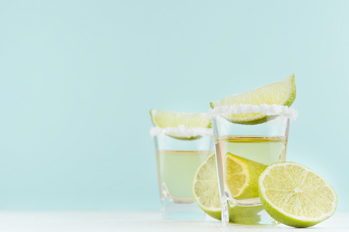 Close-up de dois copos de tequila com sal e limão em um fundo azul.