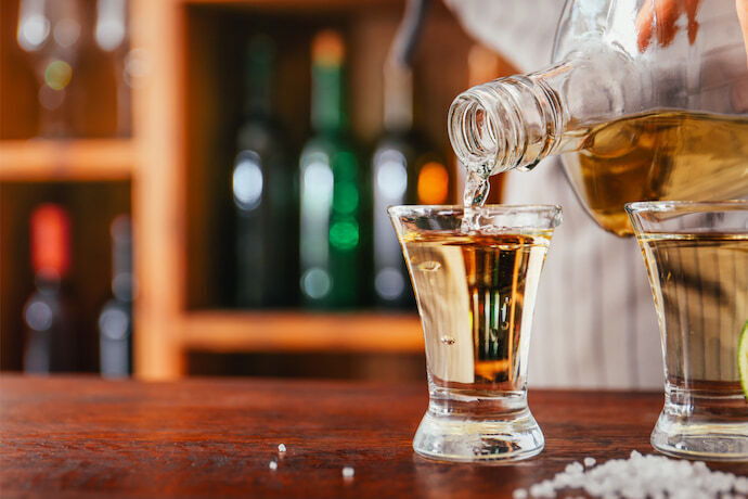 Barman servindo saborosa tequila da garrafa no vidro do balcão.