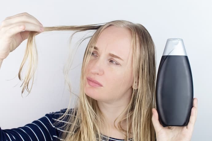 Uma mulher com um frasco de shampoo e olhando para o cabelo
