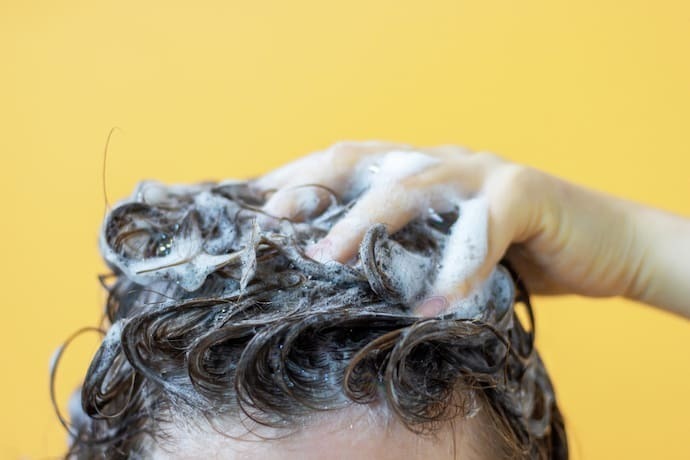 Uma garota lava o cabelo com shampoo em fundo amarelo, vista frontal