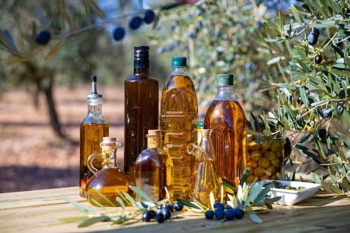 Várias garrafas em formatos diferentes com azeite de oliva com oliveiras ao fundo