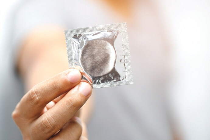 Mão segurando um pacote de preservativo