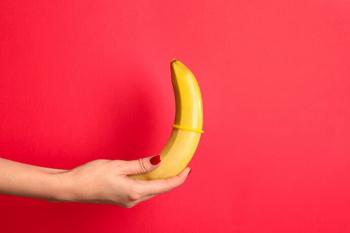 Mulher segurando banana com preservativo em fundo vermelho