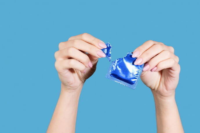 Mulher abrindo um preservativo e fundo azul