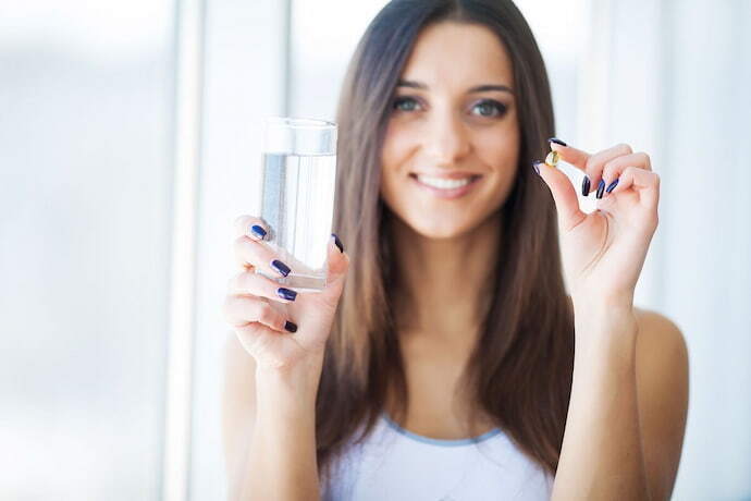 Mulher segurando copo de água e capsula de vitamina 