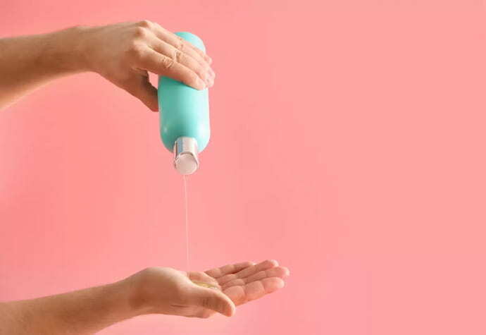 Pessoa colando shampoo na mão em cenário rosa 