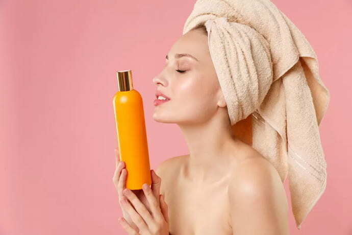 Mulher com cabelo enrolado na toalha segurando shampoo