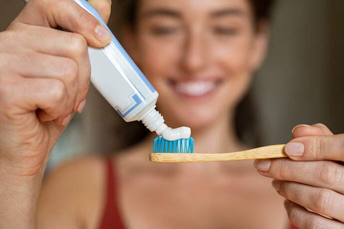Mulher aplicando pasta de dente em escova de dente de bambu