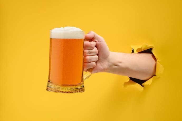 Mão em fundo amarelo segurando copo de cerveja 