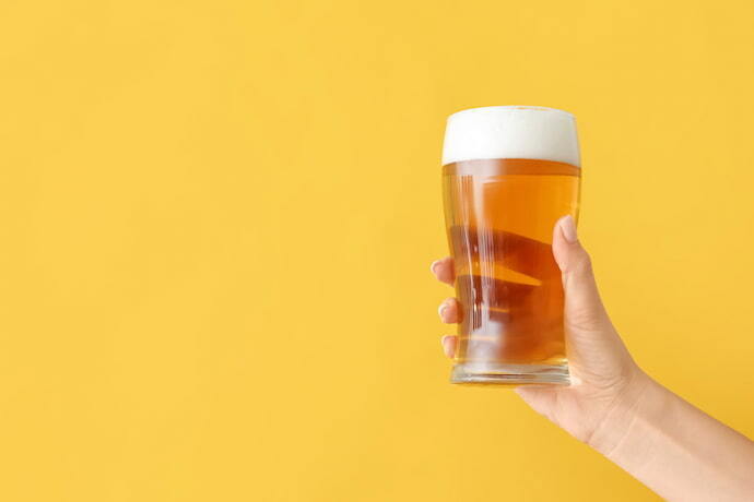 Mão segurando copo de cerveja em fundo amarelo 