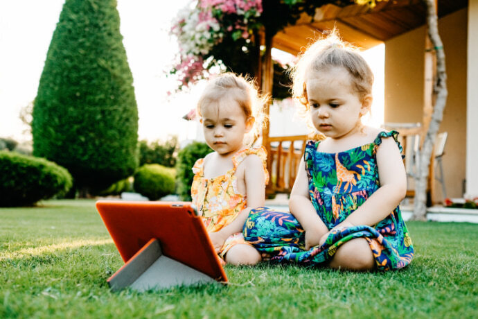 Duas meninas sentadas sobre grama e assistindo desenho no tablet