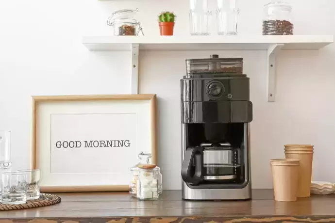 Cafeteira elétrica ao lado de quadro escrito "Bom dia"