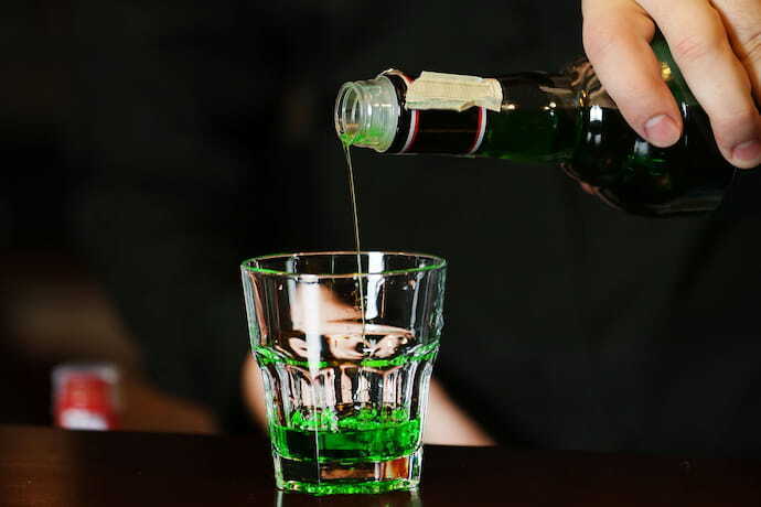 Pessoa colocando licor de cor verde em copo de shot