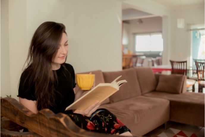 Adolescente sentada no sofá lendo livro 