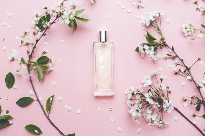 Frasco de perfume floral com flores em fundo rosa