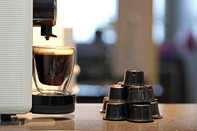 Máquina preparando café preto e cápsulas empilhadas sobre a mesa 