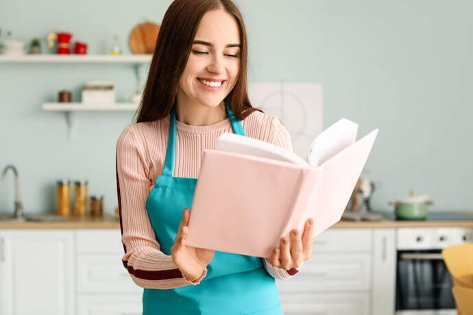 Mulher sorrindo e olhando um livro de receitas na cozinha