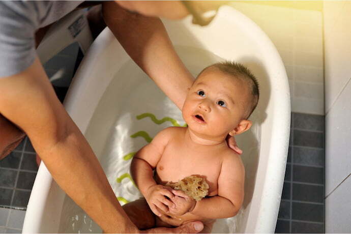 Bebê sendo banhado em banheira de plástico branco em casa