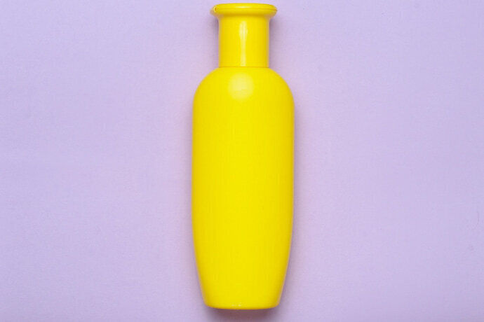 Frasco amarelo de shampoo em um fundo roxo