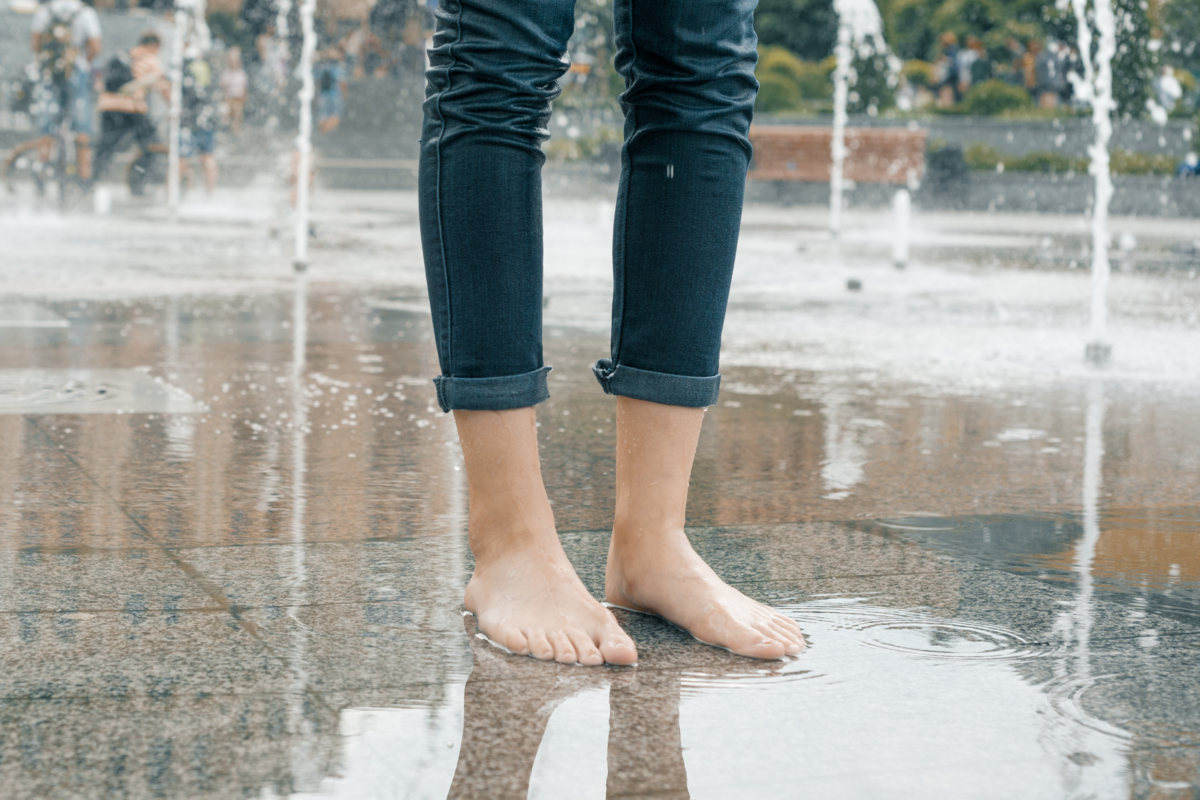 Moça com calça jeans molhada em uma praça com fontes